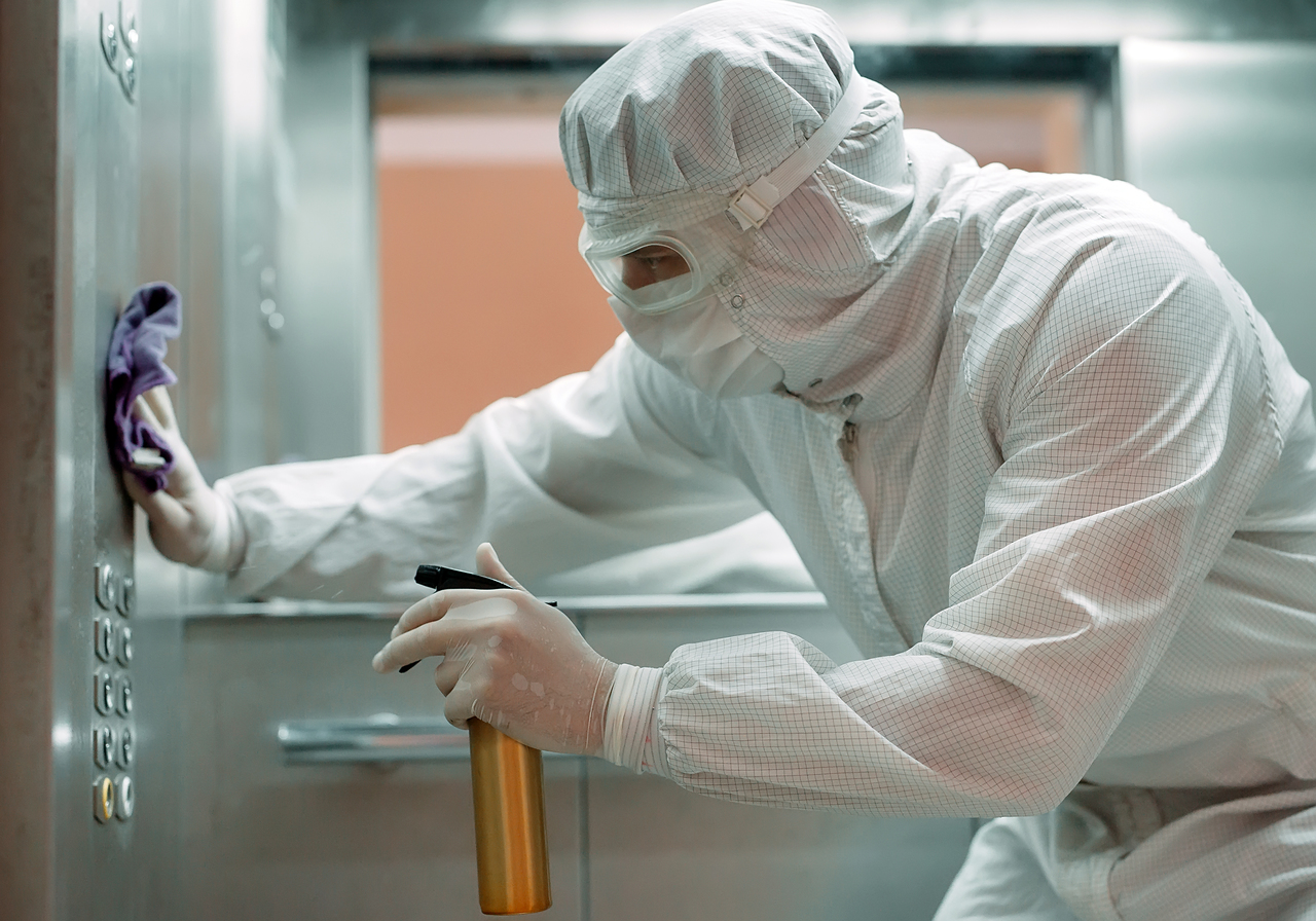 A worker in protective gear disinfecting an elevator